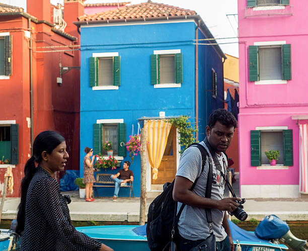 Burano, Italy. September 26, 2014. Two Indian tourists walk through the narrow streets of Burano, a small island in the lagoon of Venice, famous for its colored houses.