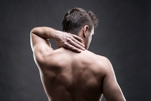 Pain in the neck. Man with backache. Muscular male body. Handsome bodybuilder posing on gray background. Low key close up studio shot. Middle part of the body