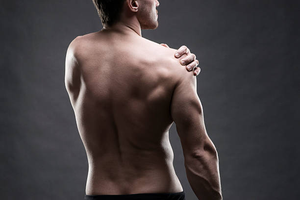 Pain in the shoulder on gray background Pain in the shoulder. Muscular male body. Handsome bodybuilder posing on gray background. Low key close up studio shot. Middle part of the body colour enhanced stock pictures, royalty-free photos & images