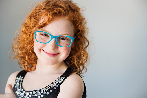 Close up head shot portrait of little brown-haired child girl. Cheerful kid against white studio wall background