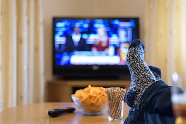 man watching TV (television) news with feet on table watching TV news with feet on table and eating snacks remote control on table stock pictures, royalty-free photos & images