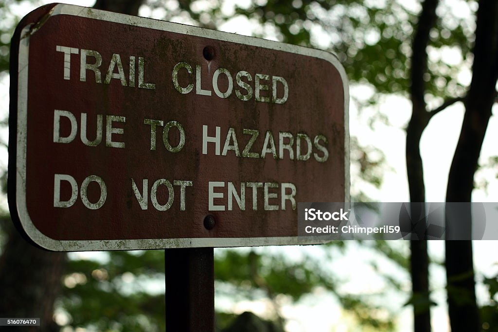 Trail Sign A trail sign at the trailhead of a hiking path states the trail is closed due to hazards Advice Stock Photo