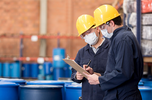 Team of workers at a chemical plant doing inventory and writing on a clipboard while wearing protective wear