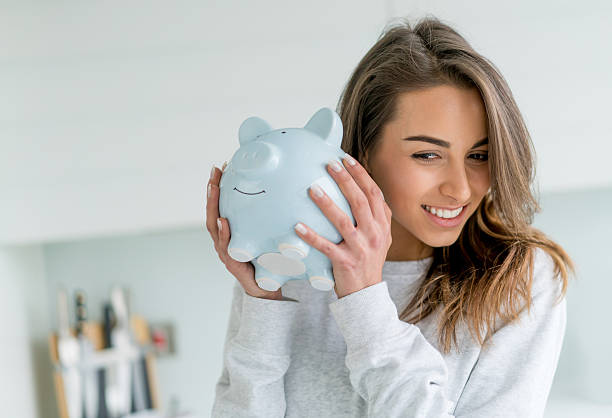 Happy woman saving money in a piggybank Happy young woman saving money in a piggybank - home finances concepts investment photos stock pictures, royalty-free photos & images