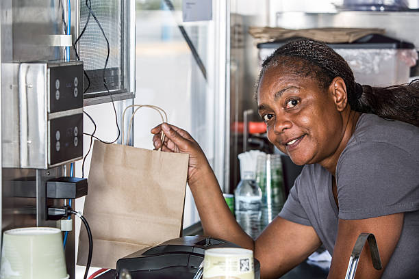 Smiling African-American Worker Hands Food Order Out Window Smiling African-American worker hands order out window of modern food truck quick service restaurant cashier stock pictures, royalty-free photos & images