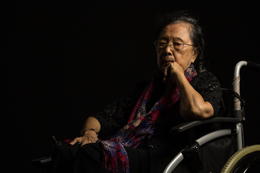 Asian elder woman in her wheelchair feeling lonely on black background