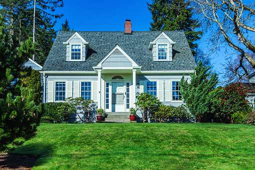 Photo of a quaint American Cape Cod Style home on a sunny day with clear blue sky and green grass.