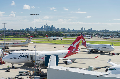 Sydney, Australia - March 4, 2013: People working on a number of airplanes on the tarmac at Sydney's Kingsford Smith Airport, with the city's skyline in the background.