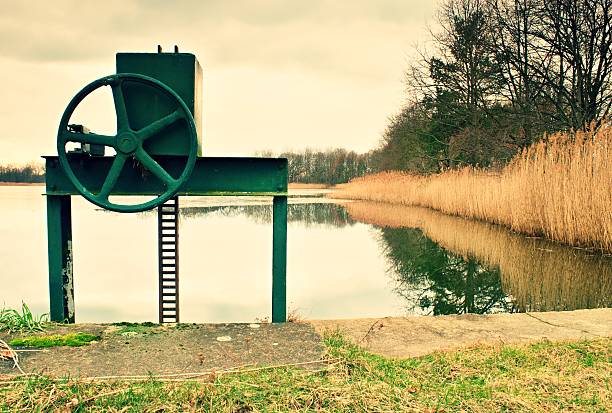 Small water reservoir, dam in autumn park. View to locked control wheel at outlet.