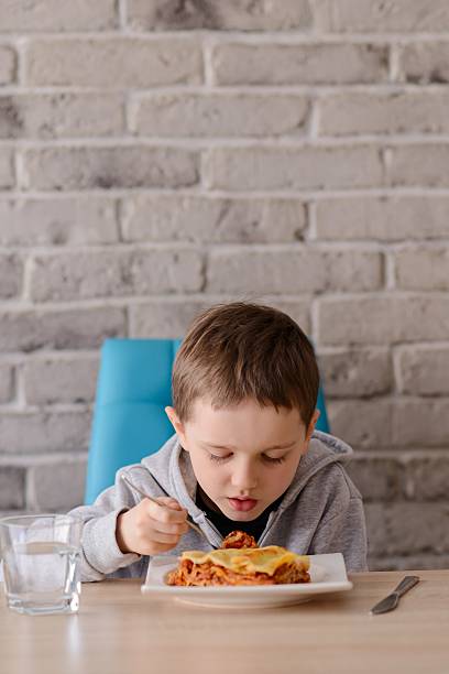 istock 7 years old boy eating lasagne in dining room 516133310