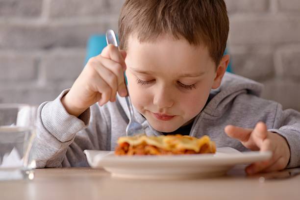 istock Seven years old boy eating lasagne in dining room 516133464