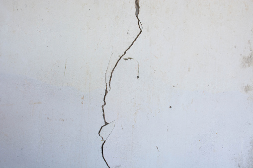 Closeup of badly fixed building facade wall covered with cracks in stucco and paint.