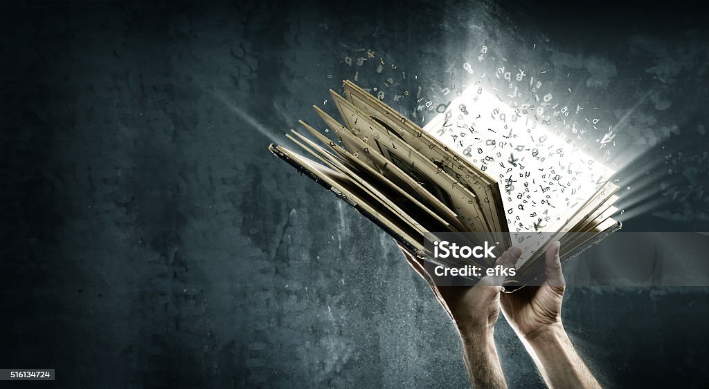 Opened magic book with magic lights Holding magic book with flying letters Book Stock Photo