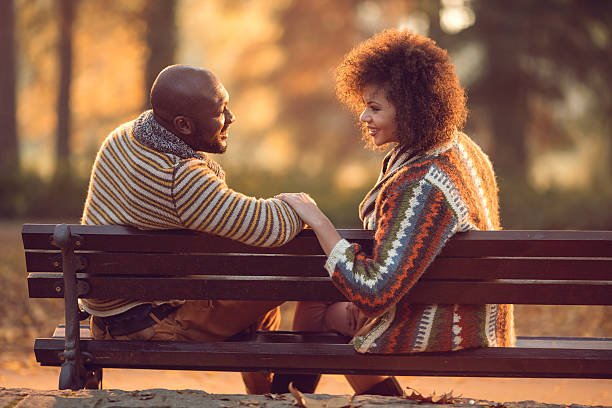 アフリカ系アメリカ人カップルでリラックスしたベンチで自然とコミュニケーションを取り合うことです。 - adult autumn couple face to face ストックフォトと画像