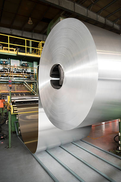 Aluminium rolled up on indutrial spool in factory Large roll of aluminium inside aluminium processing plant. Silver coloured metal on a roll inside industrial building. aluminum plant stock pictures, royalty-free photos & images