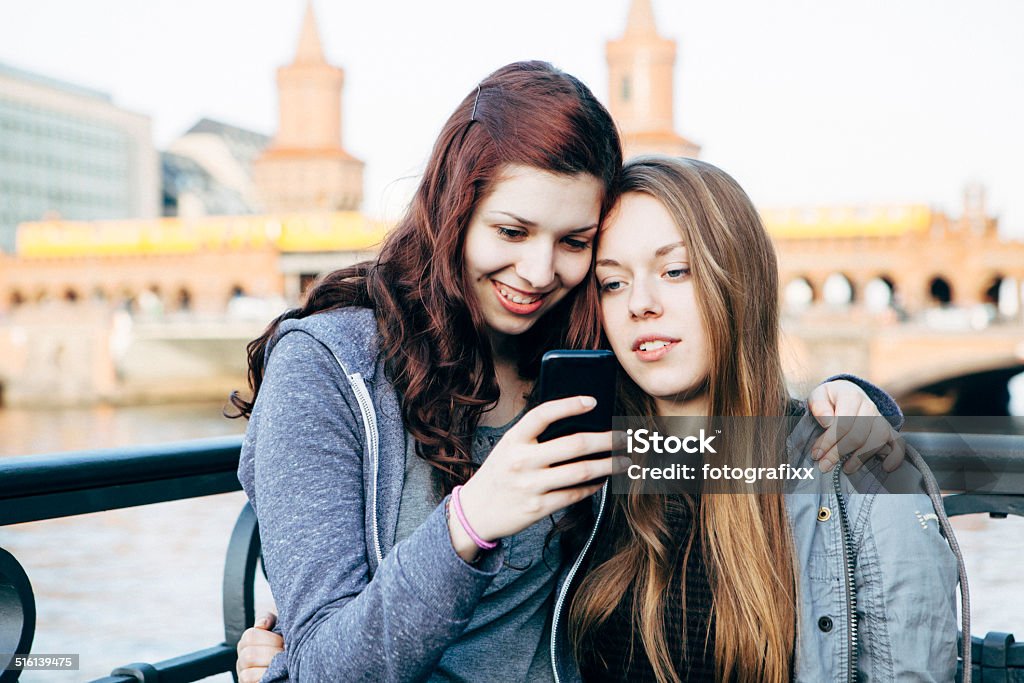 young women in the city looking into a smart phone two young women in the city looking into a smart phone, choosing music. In front of oberbaum brigde in Berlin Young Women Stock Photo