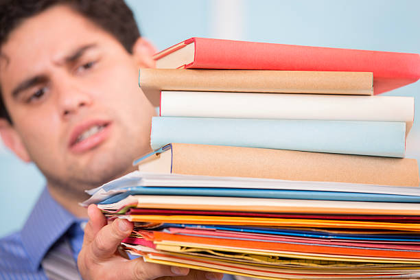 Overwhelmed Latin descent business man holding large stack of files, books, paperwork. Close up.  Office. 