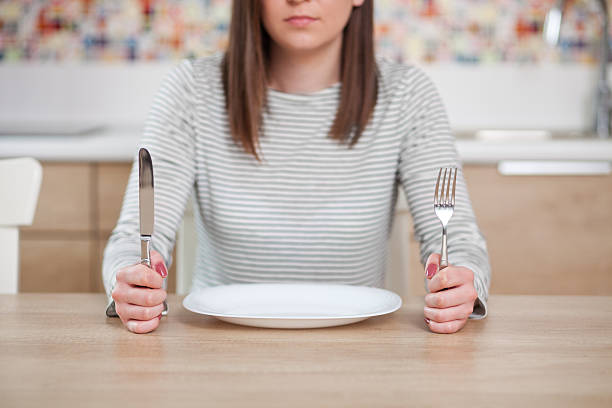 The empty plate Displeased young woman sitting at the empty plate. Shallow depth of field, focus on foreground hungry stock pictures, royalty-free photos & images