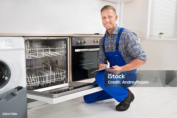 Handyman With Clipboard Looking At Dishwasher Stock Photo - Download Image Now - Adult, Appliance, Blue-collar Worker