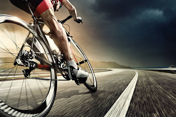 Professional road cyclist An athlete is riding a bicycle on road at the evening. The man is wearing black bike shorts and shin guards along with a red sleeveless top and a red and white helmet and sunglasses. The image is blurred in motion. racing bicycle photos stock pictures, royalty-free photos & images