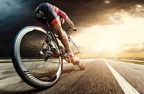 Professional road cyclist An athlete is riding a bicycle on road at the evening. The man is wearing black bike shorts and shin guards along with a red sleeveless top and a red and white helmet and sunglasses. The image is blurred in motion. crash helmet photos stock pictures, royalty-free photos & images