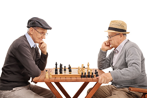 Two senior gentlemen playing chess and contemplating their next move isolated on white background