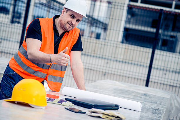 Exhausted, but satisfied! Tired construction worker at the end of his work day showing thumbs up. He is looking at camera, smiling. Building in back. He have blueprints and laptop computer in front of him. helmet hardhat protective glove safety stock pictures, royalty-free photos & images