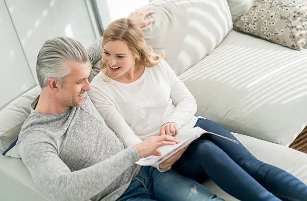 Happy couple relaxing at home reading a magazine and sitting on the couch