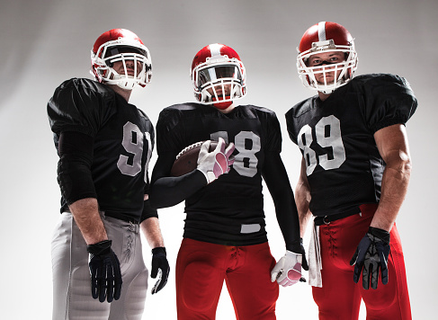 The three caucasian fitness men as american football players posing with a ball on white background