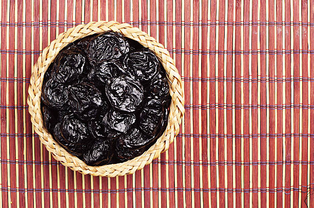 dried plum in wicker bowl - fruit table bamboo black stock-fotos und bilder