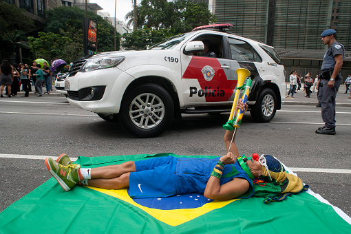 São Paulo, Brazil, March, 17, 2016: Woman dressed as a clown lying on a flag during protest on Paulista Avenue calling for an end to corruption in Brazilian politics and punishment of politicians and businessmen involved misuse of public money