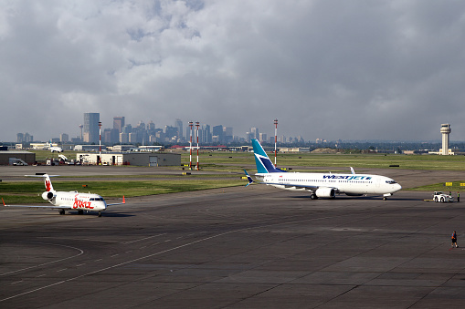 Calgary, Canada - July 18, 2014: Two commercial airliners sit on the tarmac of Calgary International Airport YYC with the city's downtown skyline in the background. The airport serves as headquarters for WestJet and as a hub airport for Air Canada.  