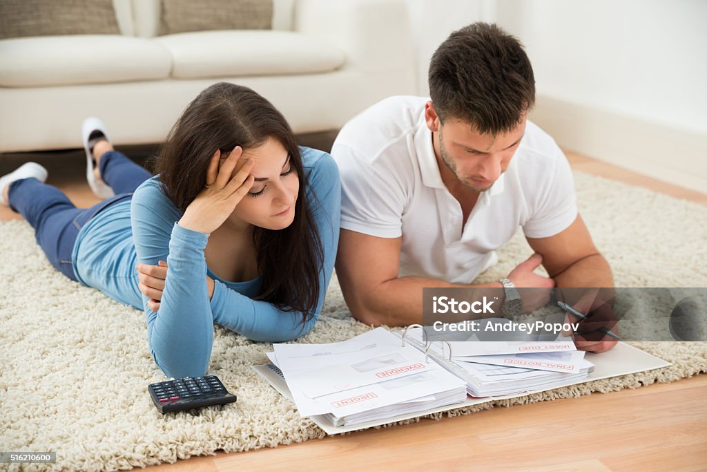 Worried Young Couple Calculating Their Bills At Home Worried Young Couple Lying On Carpet Calculating Their Bills At Home Adult Stock Photo