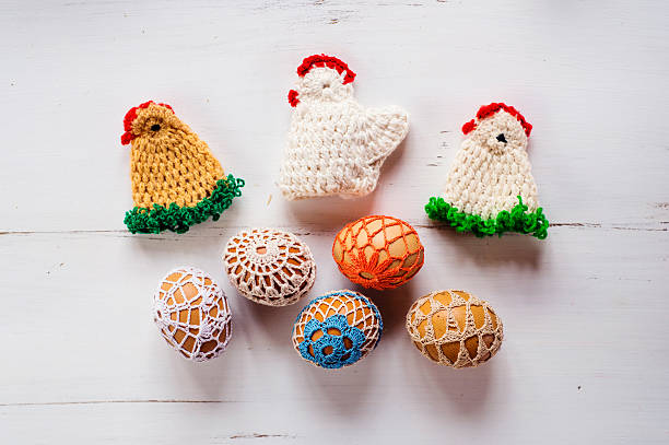 Colorful crocheted Easter chickens and eggs against white wooden background