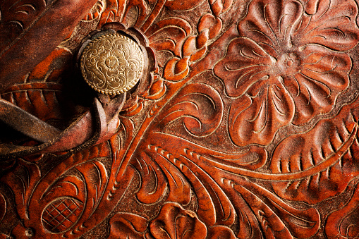 A detail of a horse saddle tooled with a filigree design reminiscent of the old west in American culture.
