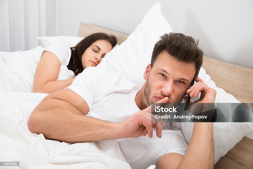 Man Talking Privately On Cellphone Man Talking Privately On Cellphone While His Wife Sleeping On Bed Infidelity Stock Photo