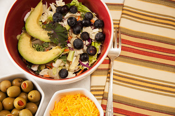 istock Mixed greens salad in bowl. Olives, cheese, fork, napkin. 516212150