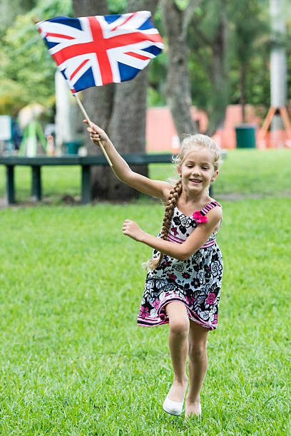 istock Young blond girl running toward camera waving British flag 516219080