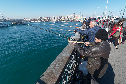 Istanbul, Turkey - March 18, 2016:Men fishing on Galata Bridge which spans the Golden Horn in Istanbul, Turkey.There behind the Galata Tower