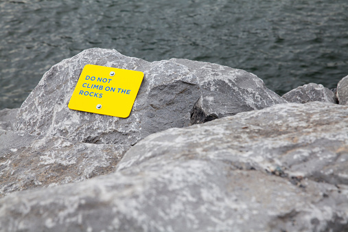 Do Not Climb On The Rocks sign at the edge of the sea