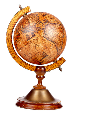 Antique globe, empty parchment, compass and quill standing on the table with library shelves on the background.