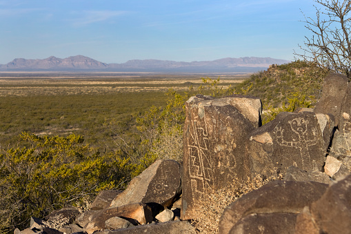 Human and geometric shaped petroglyphs remain a thousand years chipped into lava rock by Jornada Mogollon Native American at the Three Rivers Petroglyphs site with the San Andreas Mountains in the background near Alamogordo, New Mexico