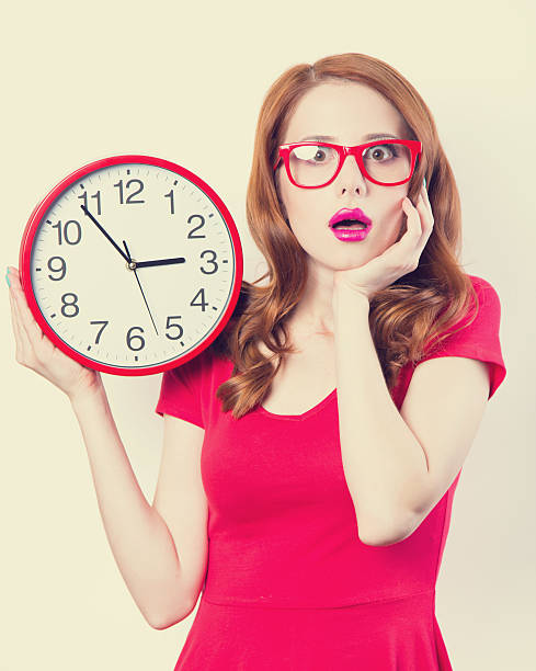 istock Surprised redhead girl with huge alarm clock on light background 516249191