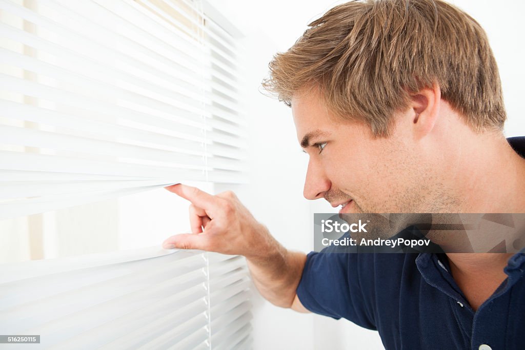 Man Peeking Through Blinds Side view of mid adult man peeking through blinds at home Adult Stock Photo