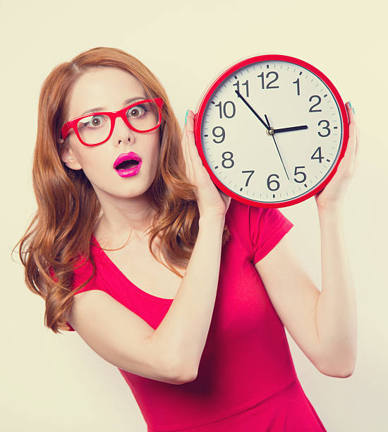 istock Surprised redhead girl with huge alarm clock on light background 516251959