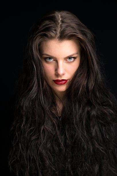 beautiful young woman with long brown hair portrait Beautiful young woman with curly brunette and very long hair looking at camera. She has big blue eyes with a touch of green in it. The portrait was shot in a studio with a black background. femme fatale stock pictures, royalty-free photos & images