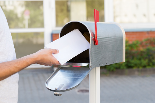Close-up Of Person Putting Stack Of Letters In Mailbox