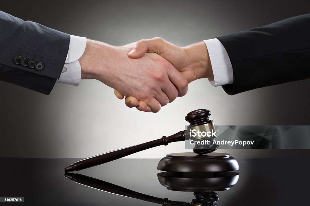 Businessman Shaking Hands In Front Of Mallet Close-up Of Two Businessman Shaking Hands In Front Of Mallet Lawyer Stock Photo