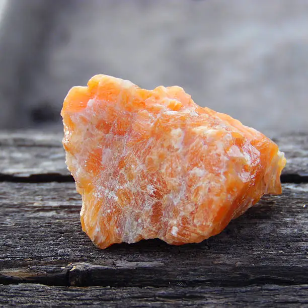 Bright rough orange calcite stone at grey natural background, closeup
