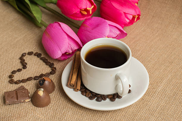 istock Coffee  cup with coffee beans on burlap and pink tulips 516261252